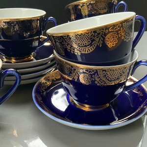 Op de afbeelding: Een set van vier blauwe en gouden theekopjes en schoteltjes. De kopjes en schoteltjes hebben een delicaat bloemenpatroon in goud op een diepblauwe achtergrond.