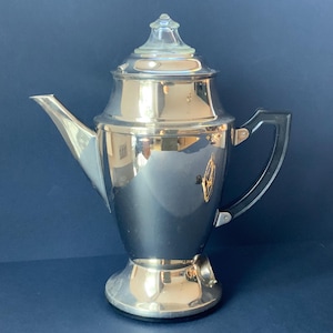 Puede incluir: Una cafetera eléctrica vintage de color plateado con un mango negro y una tapa de vidrio.