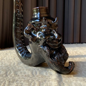 May include: A black ceramic pipe shaped like a devil's head with a top hat. The pipe has a long, curved stem and a detailed face with horns, a beard, and a mustache.