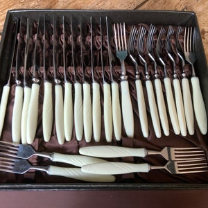 May include: A vintage set of cutlery with ivory-coloured handles, contained in a black velvet-lined case. The set includes knives and forks.
