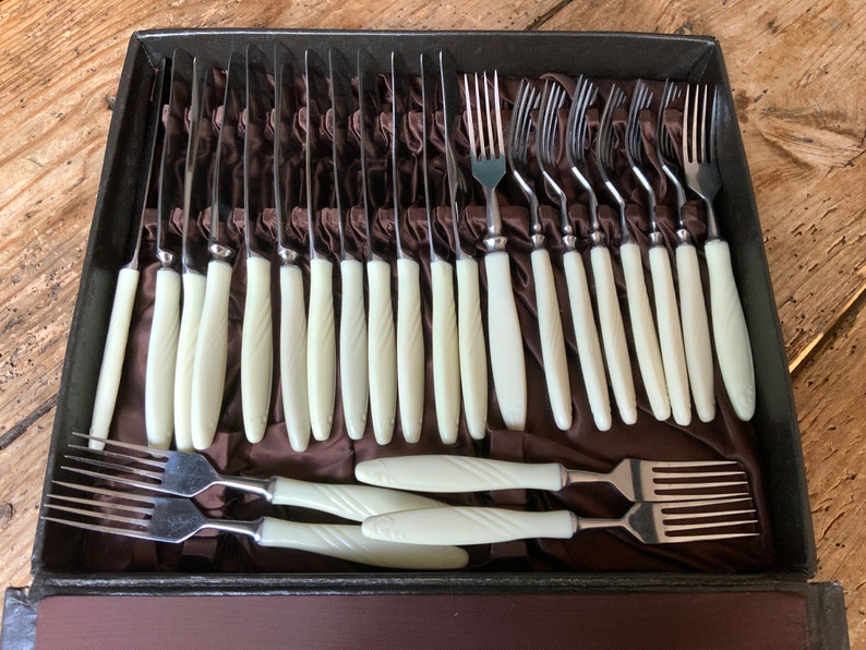 May include: A vintage set of cutlery with ivory-coloured handles, contained in a black velvet-lined case. The set includes knives and forks.