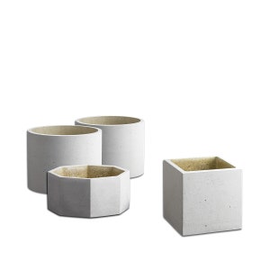Könnte beinhalten: Drei Beton-Pflanzkübel in verschiedenen Formen: zwei runde und ein quadratischer. Die Kübel sind alle in einem hellen Grauton mit einer rauen Textur.