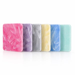 Könnte beinhalten: Ein Set aus sechs rechteckigen Acrylplatten, die in einer Reihe angeordnet sind und jeweils ein einzigartiges Marmormuster aufweisen. Die Farben umfassen leuchtendes Pink, sanftes Lila, neutrales Grau, blasses Gelb, helles Blau und Mintgrün.