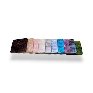 Peut inclure: Une collection de dessous de verre carrés de différentes couleurs, dont marron foncé, beige, rose, blanc, gris, bleu, violet et vert. Chaque dessous de verre présente un motif marbré ou moucheté unique, un accessoire décoratif et fonctionnel.