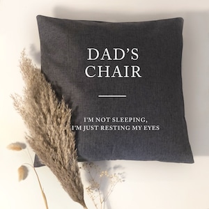 May include: A grey throw pillow with white text that reads "Dad's Chair" and "I'm not sleeping, I'm just resting my eyes".