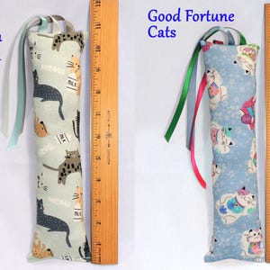 May include: Two cat-themed catnip toys with ribbons. The first toy is light blue with a pattern of black cats and milk cartons. The second toy is light blue with a pattern of white cats with good fortune symbols. Both toys are approximately 10 inches long.