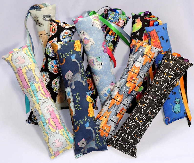 May include: A collection of colorful catnip toys with different cat designs. The toys are made of fabric and have a long ribbon attached to them. The toys are all different colors and patterns, including blue, green, yellow, orange, black, and white.