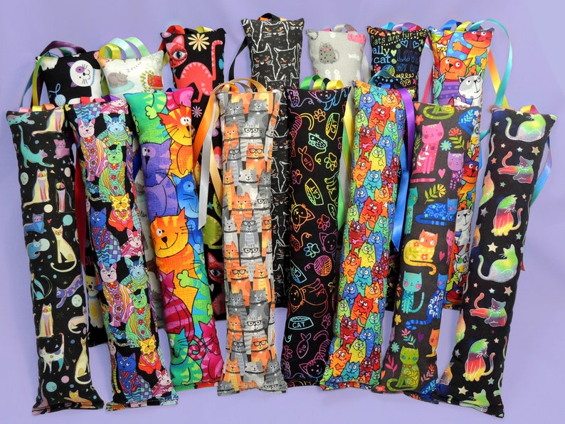 May include: A selection of catnip toys with diverse, vibrant patterns. Each long, rectangular toy displays a unique cat-themed design, such as cartoon cats and paw prints. The toys are adorned with colourful ribbons for hanging.