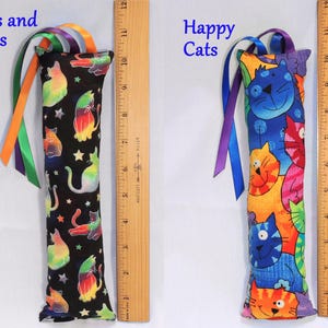 May include: Two catnip toys with colorful cat designs. The first toy is black with rainbow cats and stars and the text "Cats and Stars". The second toy is blue with colorful cats and the text "Happy Cats".