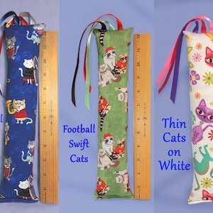 May include: Three catnip toys with colourful ribbon accents. The toys are approximately 30 cm long. One features cats on a blue background, another has cats on green, and the third has cats on white. Each toy has a different cat-themed fabric.