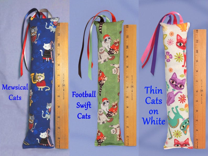 May include: Three catnip toys with colourful ribbon accents. The toys are approximately 30 cm long. One features cats on a blue background, another has cats on green, and the third has cats on white. Each toy has a different cat-themed fabric.