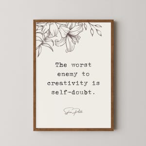 May include: A framed print with a black and white floral design at the top. The quote "The worst enemy to creativity is self-doubt." is printed in black text with the author's signature "Sylvia Plath" below.