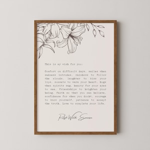 Op de afbeelding: Een ingelijst afdruk met een witte achtergrond en zwarte tekst. De tekst is een citaat van Ralph Waldo Emerson over troost, glimlachen, regenbogen, lachen en liefde. Het citaat is omgeven door een bloemmotief.