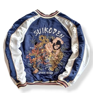 Puede incluir: Una chaqueta bomber de sat&eacute;n azul marino con mangas de sat&eacute;n blanco. La parte posterior de la chaqueta presenta un gran dise&ntilde;o bordado de un tigre y un hombre, con el texto "SUIKODEN" y "GYOJA BUSHO" en caracteres japoneses.