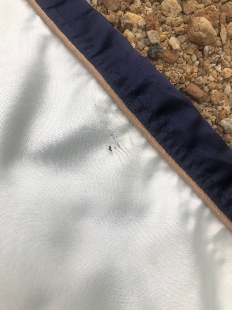 Puede incluir: Una chaqueta blanca con ribete azul marino y beige. La chaqueta tiene un peque&ntilde;o agujero cerca de la costura.