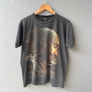 May include: A black t-shirt featuring a graphic print of a man's face with a gun and the text "Outlaw" on the front.