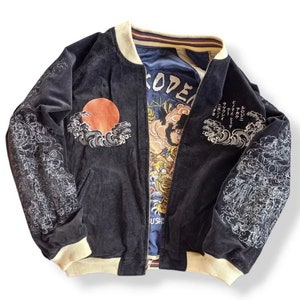 Puede incluir: Chaqueta bomber de terciopelo negro con dise&ntilde;os japoneses bordados en blanco, incluyendo olas, un sol y flores. La chaqueta tiene un cuello y pu&ntilde;os de canal&eacute; de color crema. El interior de la chaqueta est&aacute; forrado con una tela azul con texto japon&eacute;s y un gr&aacute;fico de un tigre.