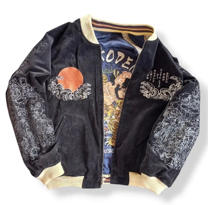 Puede incluir: Chaqueta bomber de terciopelo negro con dise&ntilde;os japoneses bordados en blanco, incluyendo olas, un sol y flores. La chaqueta tiene un cuello y pu&ntilde;os de canal&eacute; de color crema. El interior de la chaqueta est&aacute; forrado con una tela azul con texto japon&eacute;s y un gr&aacute;fico de un tigre.