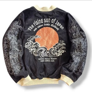 Puede incluir: Chaqueta bomber de terciopelo negro con un dise&ntilde;o bordado en blanco de un sol naciente y olas. El texto "The rising sun of Japan neo asian taste clothing" est&aacute; bordado en la parte posterior. El texto "Bakunitsu Rahman Musume eccentric folklore studio" est&aacute; bordado debajo del dise&ntilde;o. El texto "S-1916" est&aacute; bordado en el lado derecho del dise&ntilde;o.