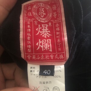 Puede incluir: Una etiqueta de ropa roja y rosa con texto japon&eacute;s que dice "Explosi&oacute;n del Este" y "Quality Goods Co., Ltd.". La etiqueta tambi&eacute;n incluye una etiqueta de talla que dice "40".