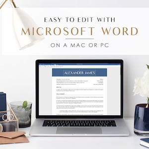May include: A laptop computer displaying a blue and white resume template with the text "Alexander James" at the top. The laptop is on a white desk with a gold lamp, a glass jar with a blue and white organizer, a glass of water, a pair of glasses, a brown leather wallet, a white bouquet of flowers, a blue candle, and a blue notebook with a pen.