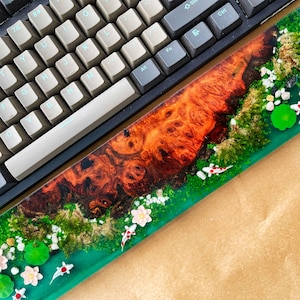 May include: A custom keyboard with a wooden wrist rest featuring a koi pond design. The wrist rest has a vibrant orange and brown wood grain pattern, with a green river and white flowers. Small koi fish swim in the river.