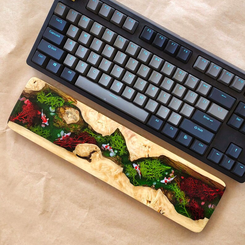 May include: A wooden keyboard wrist rest with a clear epoxy resin inlay featuring green and red swirls, and small white fish.