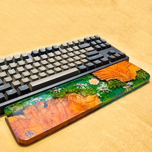May include: A black mechanical keyboard with gray keycaps rests above a wooden wrist rest. The wrist rest features a vibrant design with a green base, brown wood grain, and a floral and koi fish motif.