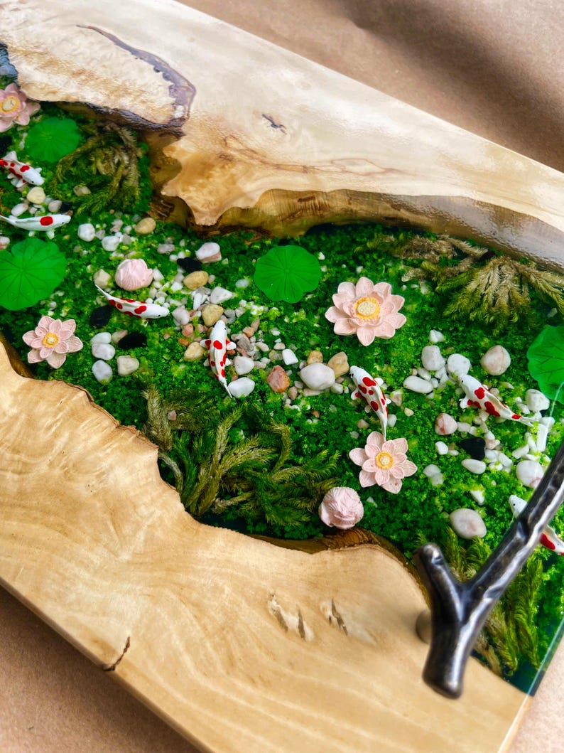 Op de afbeelding: Een houten serveerblad met een miniatuur rivierlandschap. De rivier is gevuld met groen mos, kleine stenen en miniatuur koikarpers. Roze lotusbloemen en waterlelies zijn verspreid. De lade heeft een natuurlijke houtnerf afwerking.