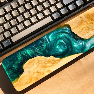 May include: A green and gold resin wrist rest with a swirling pattern. The wrist rest is made of wood and resin and has a natural wood finish.