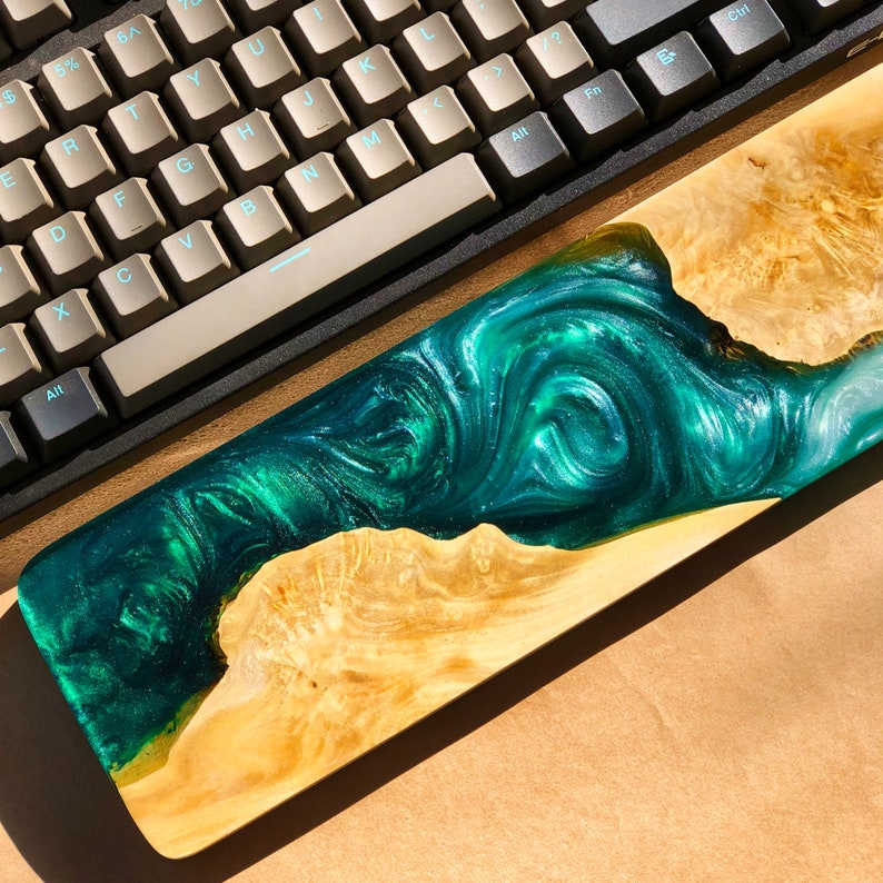 May include: A green and gold resin wrist rest with a swirling pattern. The wrist rest is made of wood and resin and has a natural wood finish.