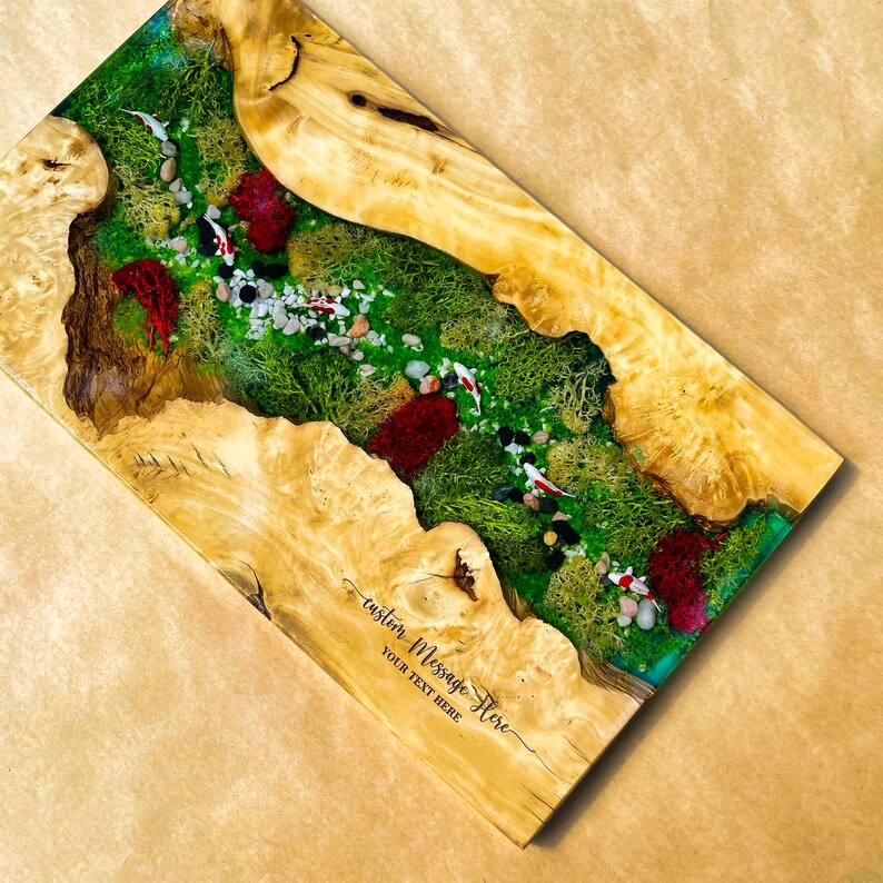 May include: A rectangular wooden art piece with a river scene. The river features green moss, small stones, and red accents, with koi fish swimming. The edges are a light-colored wood. Text on the bottom reads "custom Message Here, YOUR TEXT HERE."