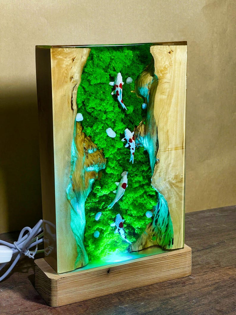 May include: A rectangular wooden lamp with a resin interior featuring a green moss landscape and miniature koi fish. The lamp has a wooden base and a light cord.