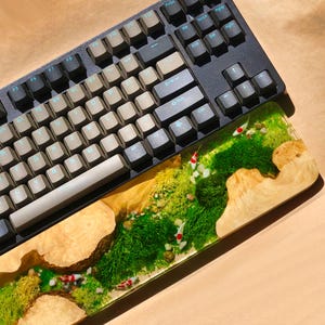 Puede incluir: Un reposamu&ntilde;ecas de madera para teclado con una parte superior de resina epoxi transparente. La resina contiene musgo verde y peque&ntilde;os peces blancos. El reposamu&ntilde;ecas est&aacute; sobre un teclado negro y gris.