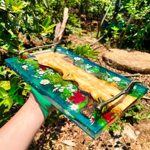 May include: A rectangular serving tray with a clear, turquoise resin base. The tray features a natural wood centerpiece, miniature koi fish, and floral accents. The tray has bronze-colored handles.