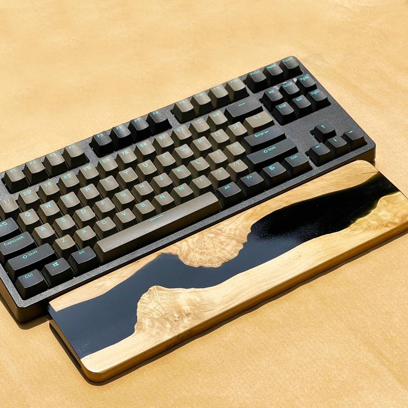 K&ouml;nnte beinhalten: Eine schwarze mechanische Tastatur mit hellgr&uuml;ner Beschriftung liegt &uuml;ber einer h&ouml;lzernen Handgelenkauflage. Die Handgelenkauflage zeigt einen Fluss aus schwarzem Harz, der durch helles Holz flie&szlig;t und ein einzigartiges Design schafft.