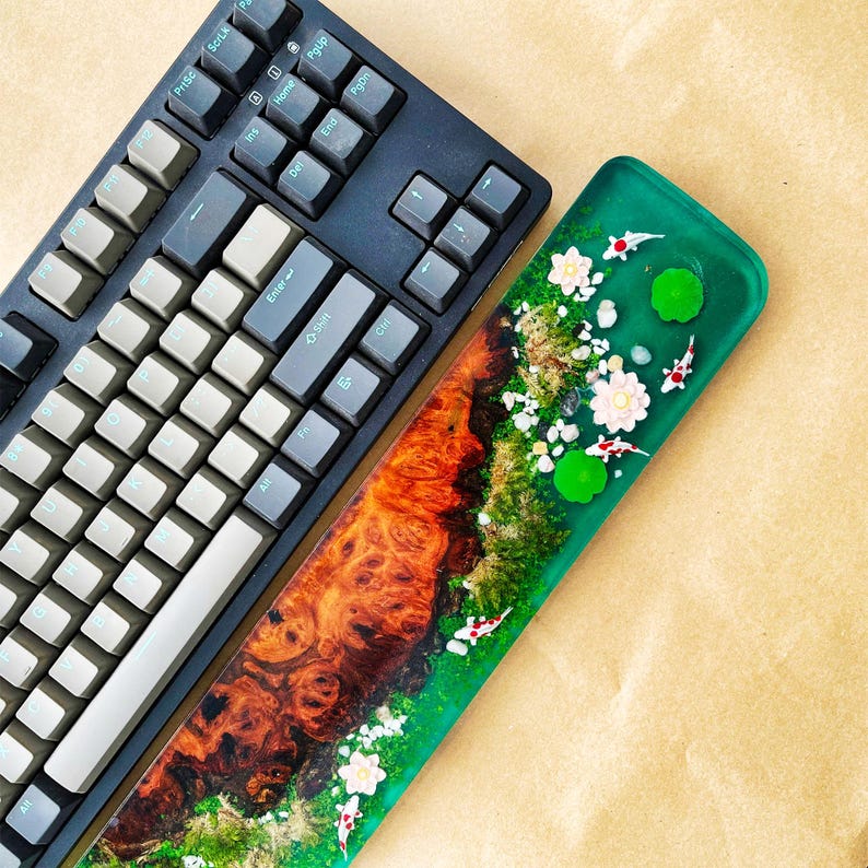 May include: A black mechanical keyboard with gray keycaps sits next to a custom resin wrist rest. The wrist rest features a vibrant design with koi fish, white flowers, and green lily pads set against a green background.