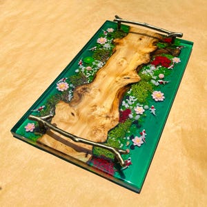 May include: A rectangular serving tray with a vibrant green resin base. The tray features a natural wood centerpiece, surrounded by miniature plants, flowers, and koi fish. Gold-toned handles are attached to the sides.