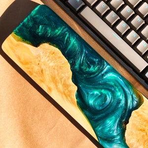 May include: A wooden keyboard wrist rest with a green and blue epoxy resin inlay. The resin has a swirling pattern and a glittery finish.