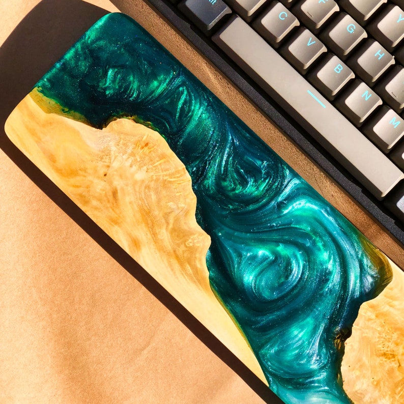 May include: A wooden keyboard wrist rest with a green and blue epoxy resin inlay. The resin has a swirling pattern and a glittery finish.