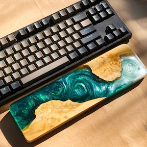 May include: A wooden keyboard wrist rest with a green and white epoxy resin design. The resin has a swirling pattern, resembling water.
