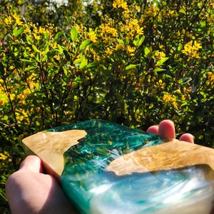 May include: A rectangular serving tray made of wood and resin. The resin is a light blue and green color, creating a wave-like pattern. The wood is a light brown color.