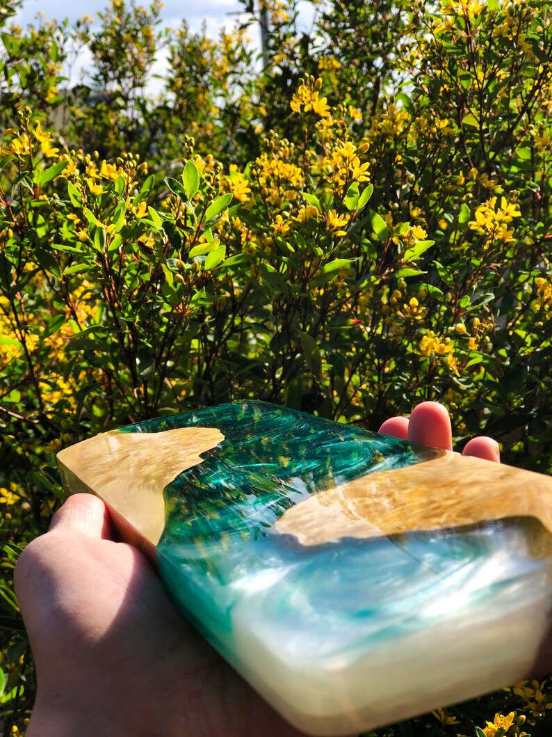 May include: A rectangular serving tray made of wood and resin. The resin is a light blue and green color, creating a wave-like pattern. The wood is a light brown color.