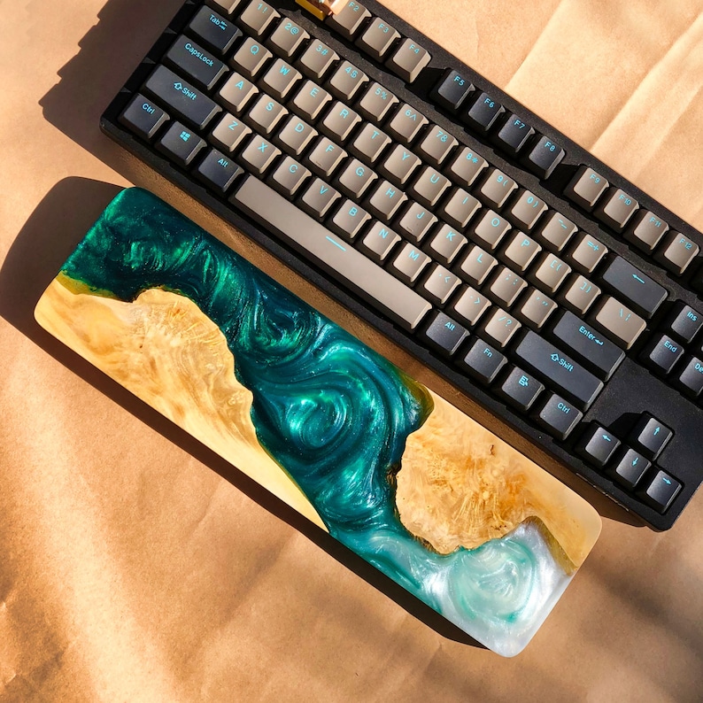 May include: A wooden keyboard wrist rest with a green and blue epoxy resin design. The resin looks like a river flowing through a forest.