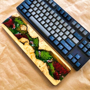 May include: A wooden keyboard wrist rest with a resin inlay featuring a river scene with green moss, red coral, and white fish.