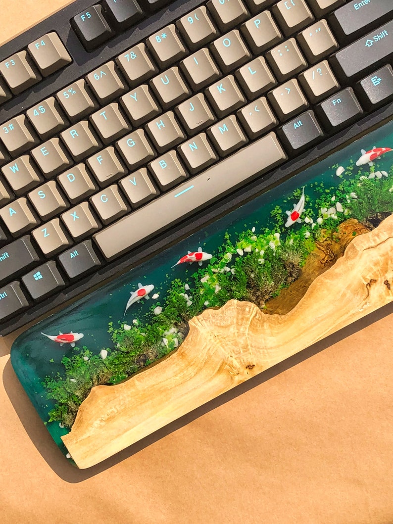 May include: A wooden keyboard wrist rest with a clear epoxy resin top. The resin contains green moss, white rocks, and red and white koi fish.