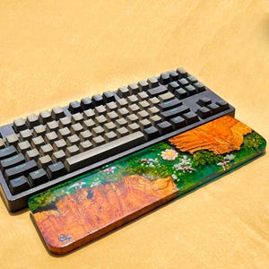May include: A black mechanical keyboard with gray keycaps rests above a wooden wrist rest. The wrist rest features a vibrant epoxy resin design with a koi pond scene, showcasing orange wood grain, green resin, and white and red koi fish.