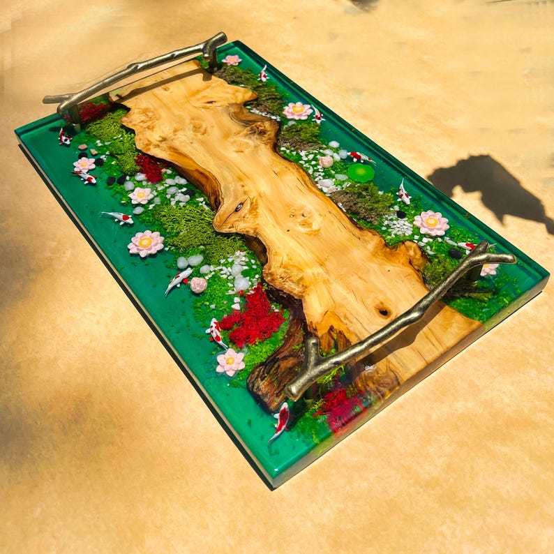 May include: A rectangular serving tray with a vibrant green resin base. The tray features a natural wood centerpiece, miniature koi fish, and floral accents. The tray has metal branch handles.