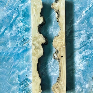 Puede incluir: Dos tablas de madera de color claro con un borde natural y un canal oscuro e irregular que recorre el centro. La madera tiene un color marr&oacute;n claro con acentos marrones y negros m&aacute;s oscuros. El fondo es un patr&oacute;n de m&aacute;rmol azul.