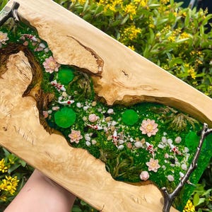 Op de afbeelding: Een rechthoekig houten kunstwerk met een miniatuurvijver. De vijver is gevuld met groen mos, kleine steentjes, waterlelies en roze bloemen. Verschillende koikarpers zwemmen in het water. Het houten frame heeft een natuurlijke houtnerf.
